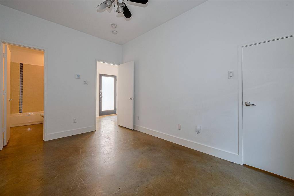 This room features polished concrete floors, white walls, and a ceiling fan. It includes a bathroom and offers access to an outdoor area through a door with frosted glass.
