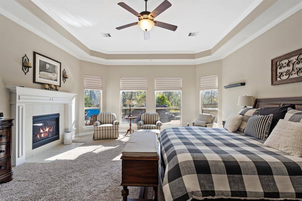 Additional view of the primary bedroom suite, highlighting the inviting bay window and serene pool view. Crown molding and high ceilings add sophistication, while the cozy fireplace adds additional comfort to this space.