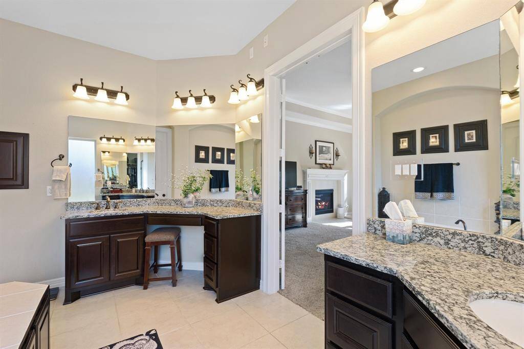 Luxurious primary bathroom with a double vanity, sleek granite countertops, a seamless mirror, and built-in storage. A sitting area at the vanity adds both function and comfort.