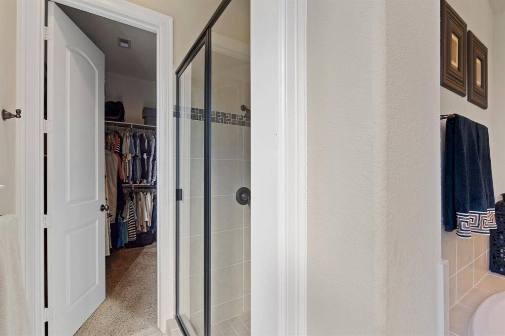 Walk-in shower and oversized closet with generous storage space and built-in shelves, adding to the home’s luxury features. Neutral finishes throughout the bathroom and closets create a timeless, tranquil ambiance.
