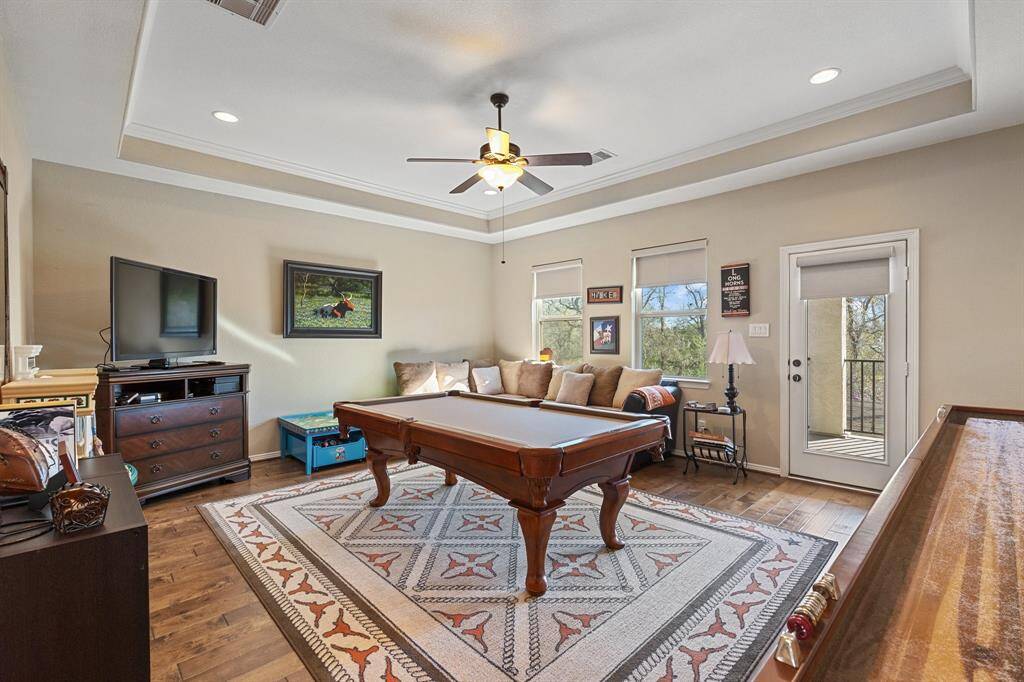 Spacious secondary living area on the second floor is designed for both relaxation and entertainment. With access to the charming balcony, it offers a seamless indoor-outdoor connection and breathtaking views of the wooded landscape. The tray ceiling adds architectural elegance, while the rich wood flooring enhances the room's warmth. This space is perfect for family gatherings, game nights, or simply unwinding in style.