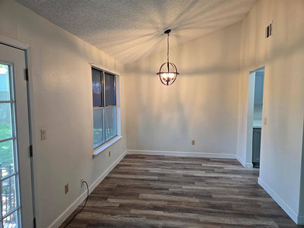 This room features a modern light fixture, wood-look flooring, and neutral walls. It has a large window for natural light and an adjacent door leading outside, creating a bright and inviting space.