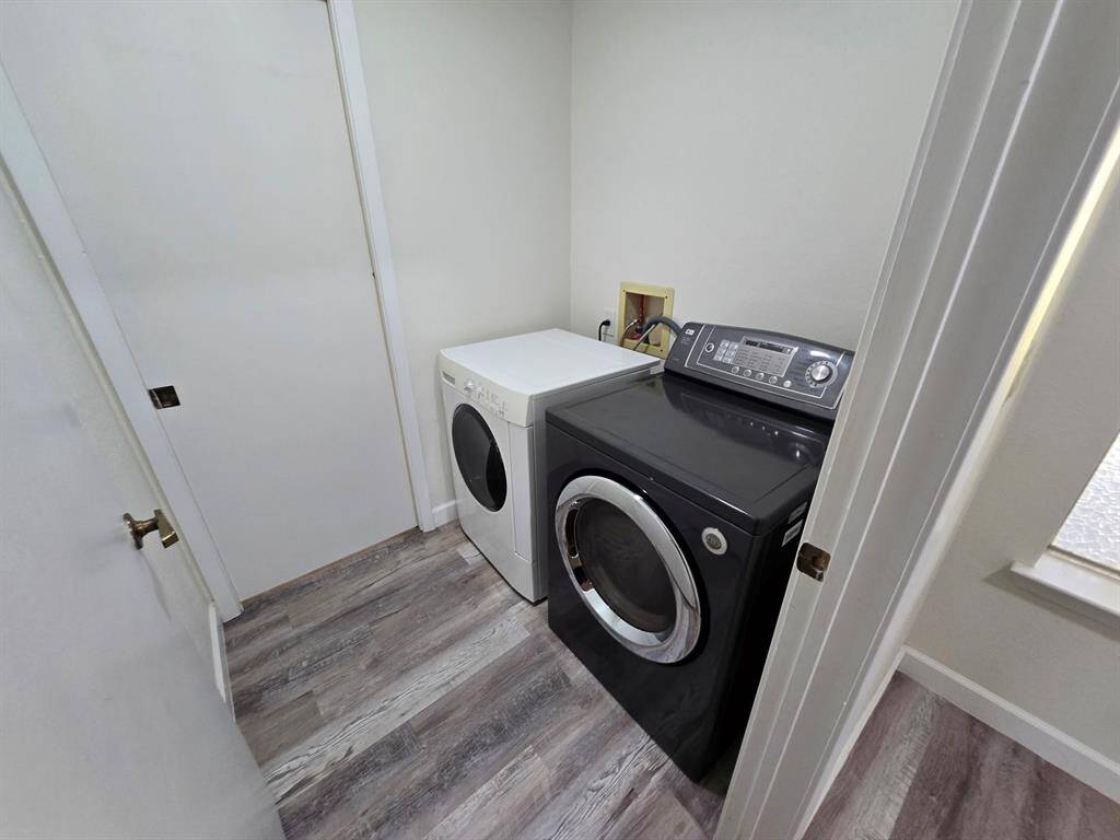 This photo shows a compact laundry room with a modern washer and dryer. The space features light-colored walls and wood-style flooring, offering a clean and functional area for laundry tasks.