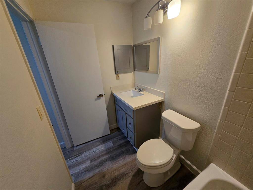 This bathroom features a modern vanity with storage, a mirror cabinet, and overhead lighting. It includes a toilet and a bathtub with a tiled wall. The space has a clean, neutral color scheme and updated flooring.