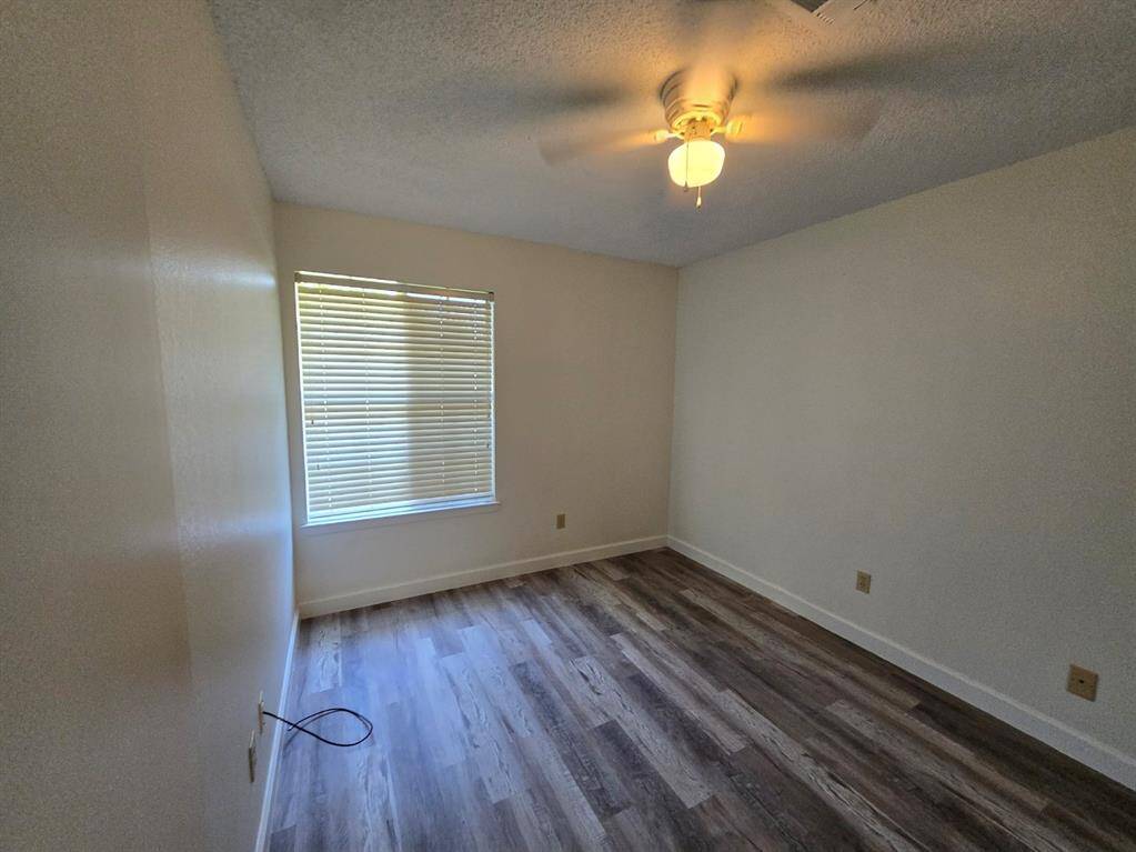 This room features neutral walls, wood-style flooring, a ceiling fan with light, and a window with blinds providing natural light.