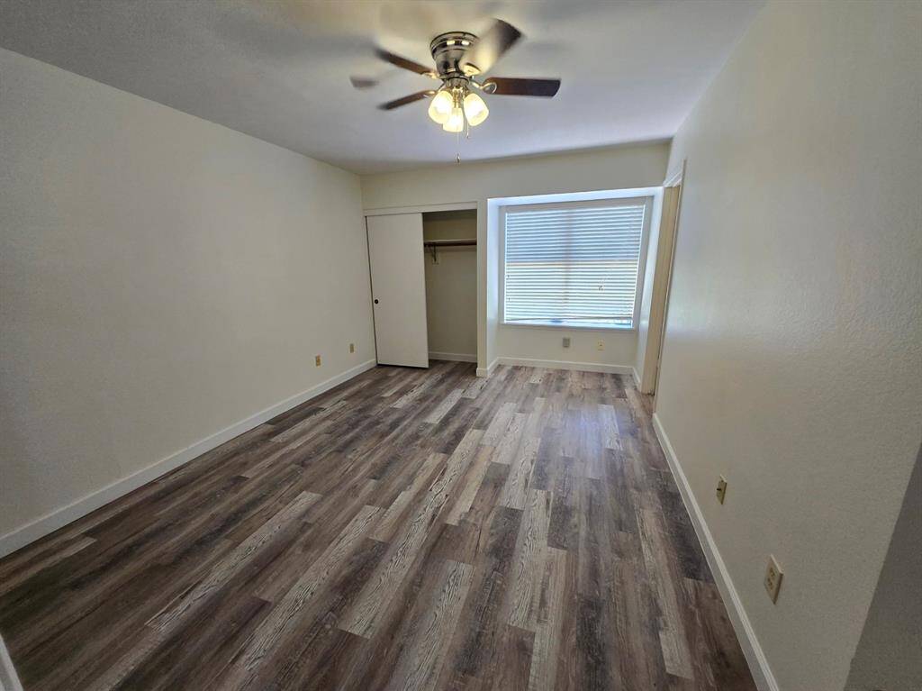 This bedroom features wood-style flooring, a ceiling fan with light, and a large window allowing natural light. It includes a closet with sliding doors, creating a functional and inviting space.