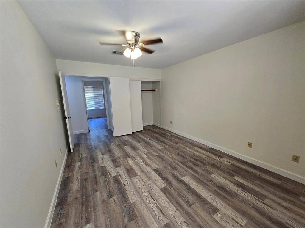 This room features wood-style flooring, a ceiling fan, and a neutral color scheme. It includes a closet with sliding doors and an adjacent space with a window, allowing for natural light.
