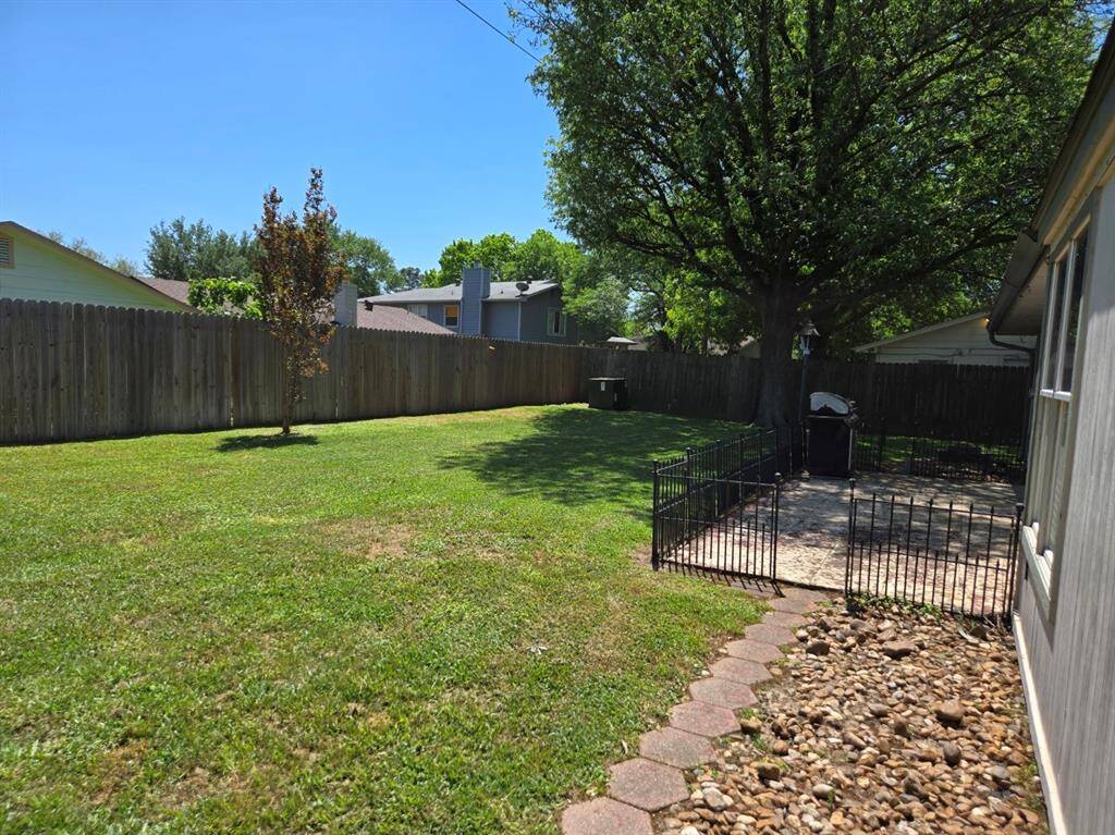 Spacious backyard with a well-maintained lawn, mature trees, and a wooden privacy fence. Includes a paved patio area with a small fence, perfect for outdoor activities and relaxation.