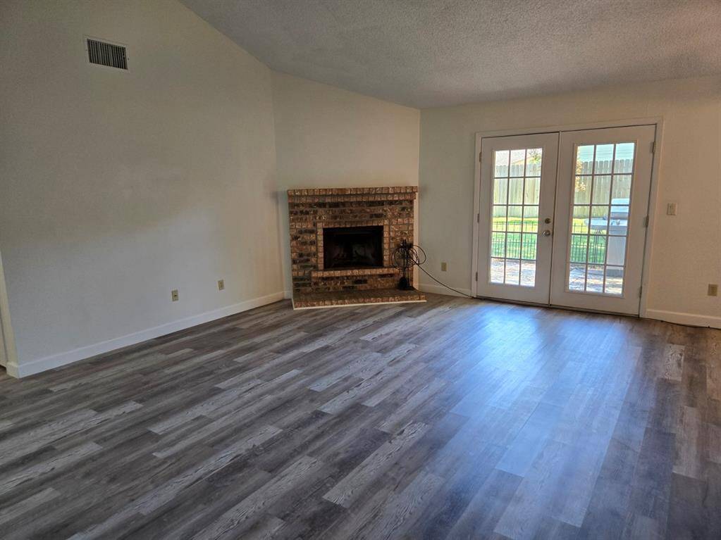 This spacious living area features elegant wood flooring, a cozy brick fireplace, and French doors leading to a fenced backyard, providing ample natural light.