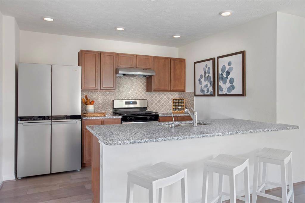 The view of this gorgeous kitchen showcases high ceiling, recessed lighting, engineered wood flooring, SS appliances, granite countertops, beautiful tile backsplash, and Woodmont Cody cabinets! NOTE: artwork will be sold with home.
