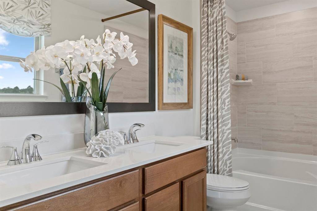 The primary bathroom features tile flooring, bath/shower combo with tile surround, stained wood cabinets, dual vanity sinks, light countertop, framed mirror, and Moen chrome bathroom faucets!