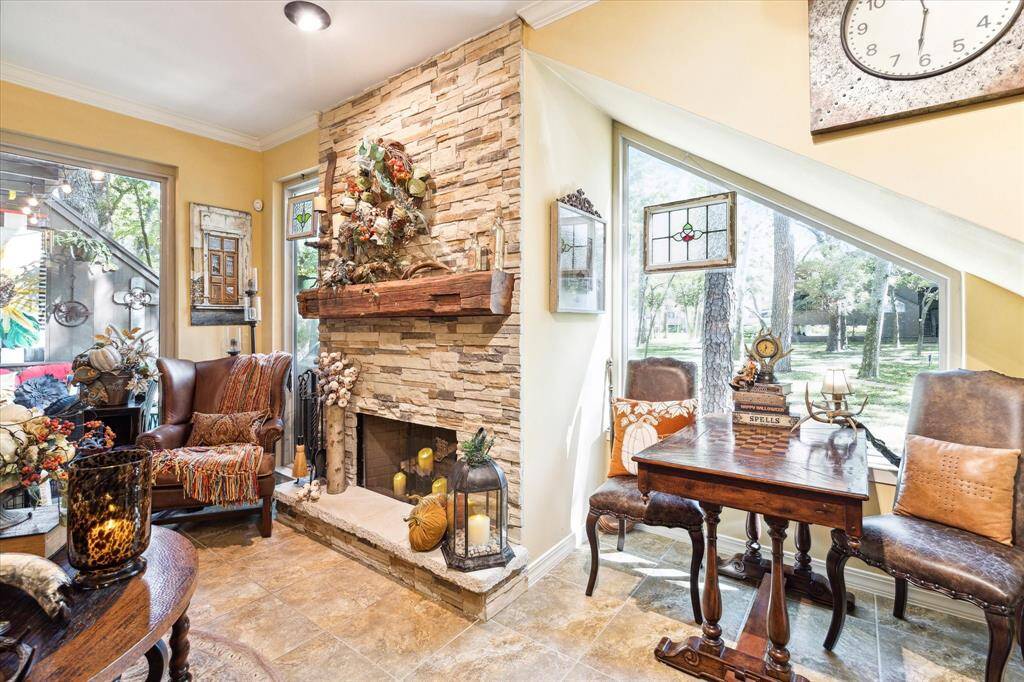 This is a cozy, well-lit living room featuring a stone fireplace, large windows, and a wooden entertainment center. The decor is rustic with warm tones and comfortable seating, creating an inviting atmosphere.