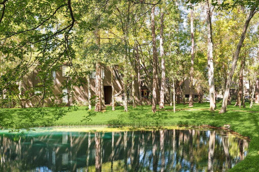 This serene setting features a beautiful pond surrounded by lush trees with a house peeking through the foliage, offering a tranquil and private living space.