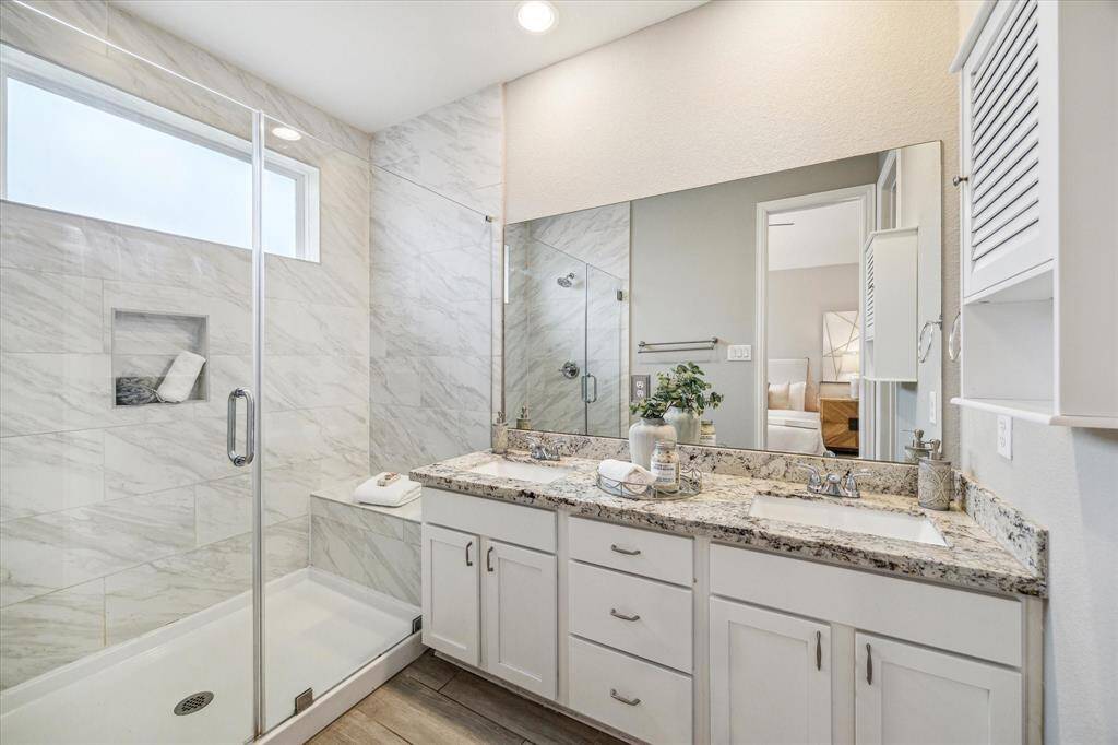 Primary bathroom features dual sinks and a glass stand up shower.