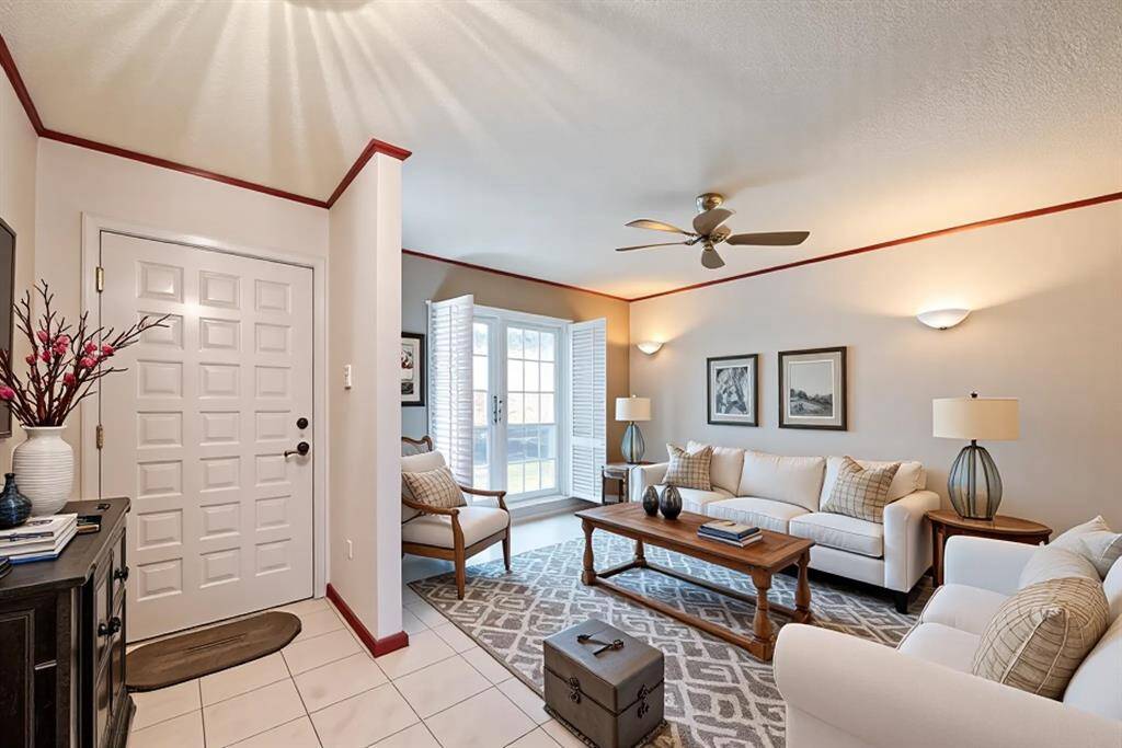 Step into the inviting formal living room, where natural light pours in through classic plantation shutters, highlighting the warm tones and clean lines of this beautifully arranged space. Virtually staged to showcase its full potential, this room features neutral walls with bold trim accents, sleek tile flooring, and plenty of room to gather, relax, or entertain with ease.