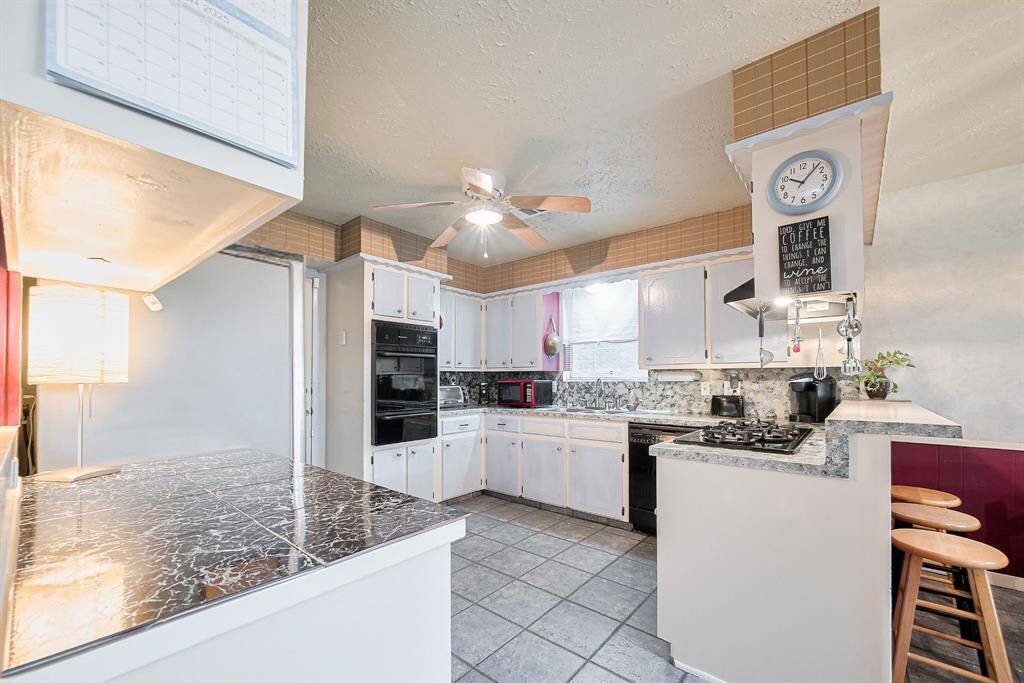 This spacious kitchen offers tons of prep space, vintage charm, and functionality with a wraparound layout. Featuring a gas cooktop, double ovens, and a breakfast bar with seating, it's designed for both everyday living and entertaining. The tile floors and ample cabinet storage make it as practical as it is inviting—ready for your personal touch or easy updates over time.