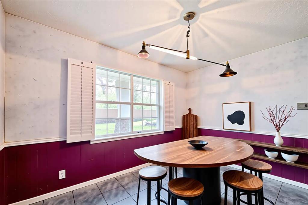 Enjoy casual meals or morning coffee in this bright and cheerful breakfast nook, virtually staged to highlight its potential. With large windows, charming shutters, and statement lighting, the space is full of character and natural light. The bold wall color adds a playful touch, creating a cozy yet modern dining experience just off the kitchen.