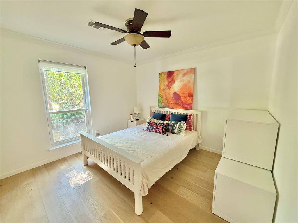 This bright bedroom features a large window with natural light, a ceiling fan, and light wooden flooring.