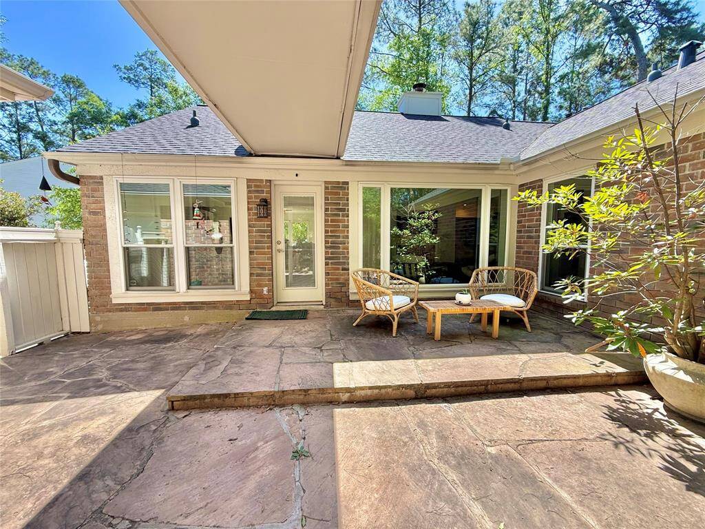 This photo showcases a charming outdoor patio area with a spacious stone surface, cozy seating, and a backdrop of brick walls. Large windows provide ample natural light, and the space is surrounded by greenery.