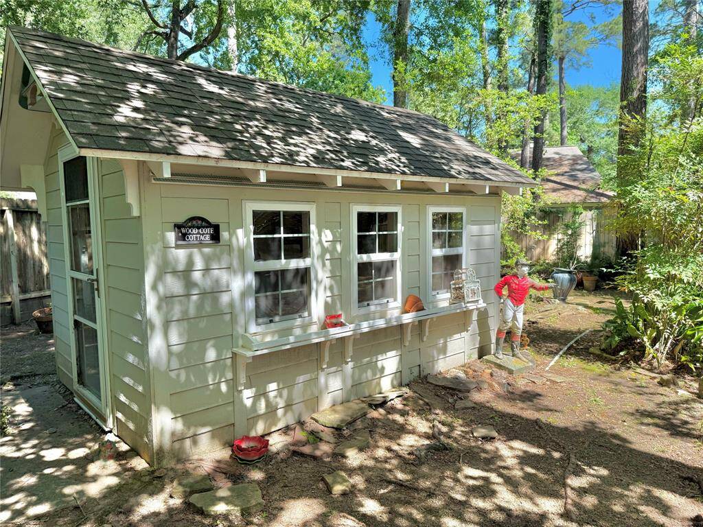 Charming backyard cottage surrounded by lush greenery, featuring a quaint exterior with a shingled roof, multiple windows. Perfect for a cozy retreat or garden workshop.