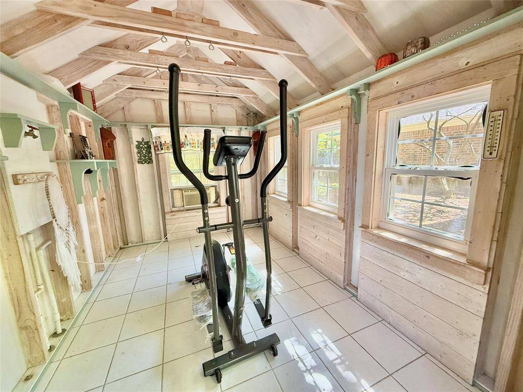 This cozy room features a rustic wooden interior with high ceilings and large windows with an AC unit, offering abundant natural light. Also perfect for a home gym setup.
