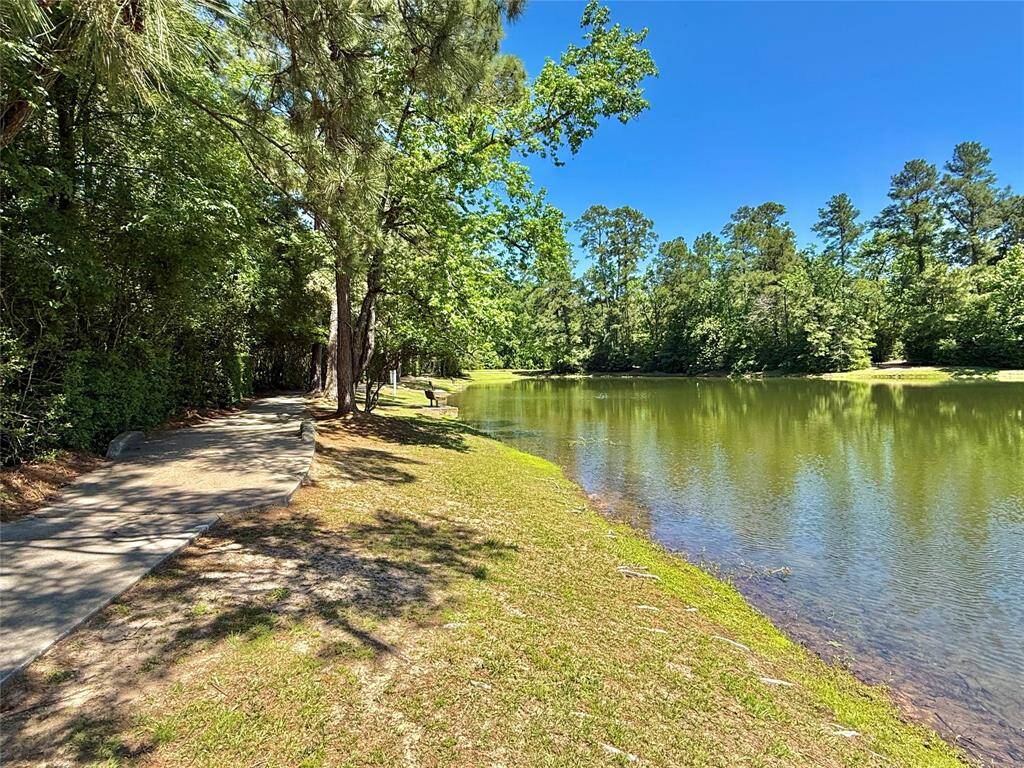 This serene photo features a scenic walking path alongside a tranquil pond, surrounded by lush greenery and tall trees, offering a peaceful natural setting perfect for outdoor relaxation and leisurely strolls.
