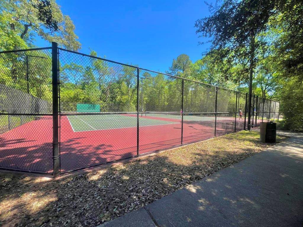 This photo shows a well-maintained outdoor tennis court surrounded by lush greenery, offering a recreational space for residents.