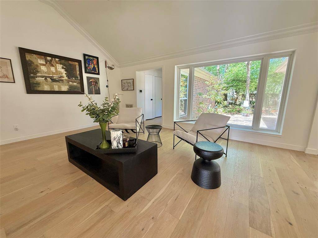 This bright living room features hardwood floors, large windows with a view of greenery, offering a serene and stylish space.