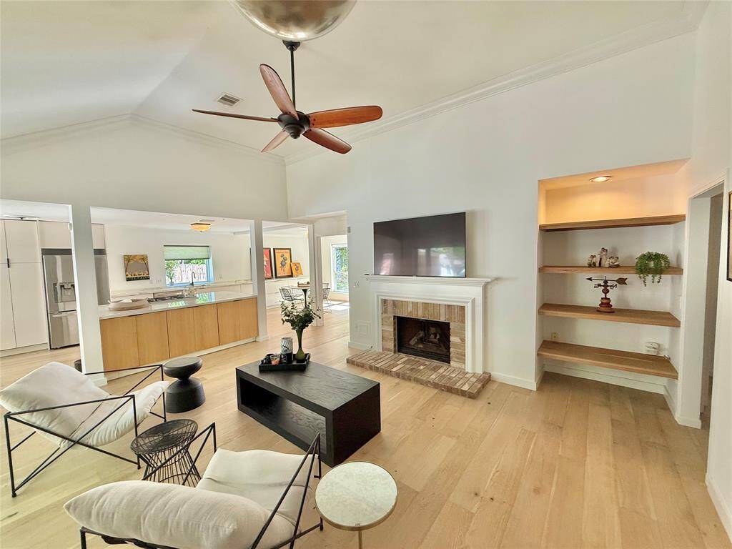 Bright, open-concept living space featuring a modern kitchen with a large island, a cozy living area with a fireplace, and stylish built-in shelves. The high ceilings and light wood flooring enhance the spacious feel.