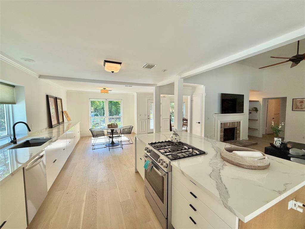 This open-concept kitchen and living area features modern design with light wood flooring, sleek white cabinetry, and a porcelain slab island with a gas stove.