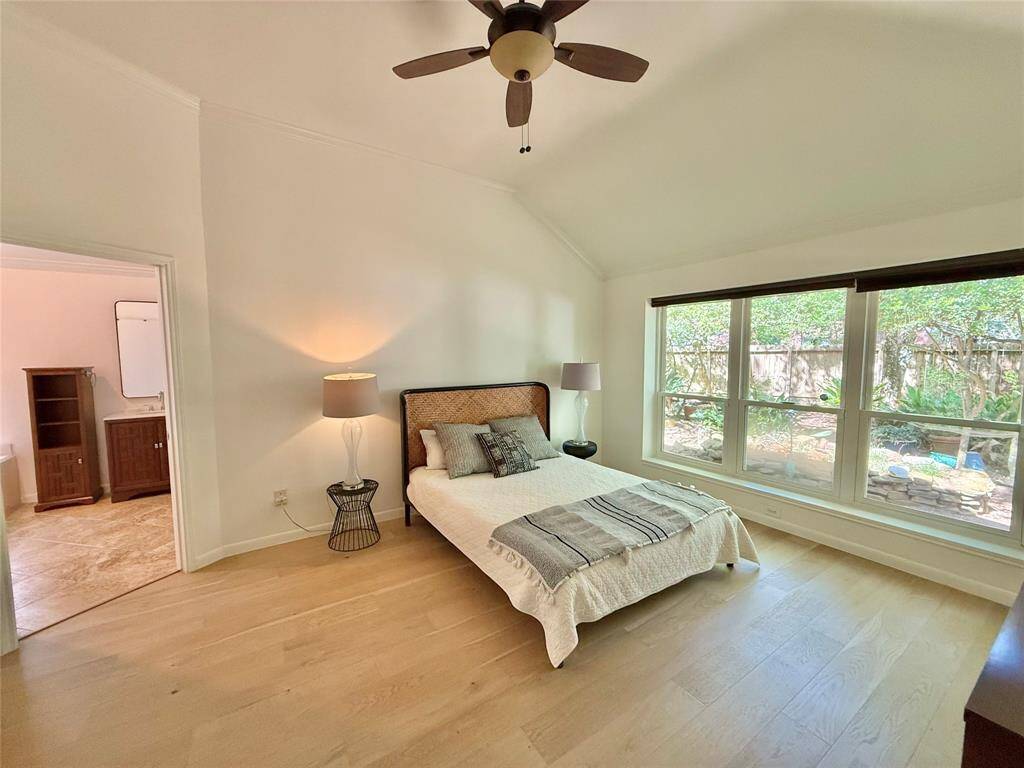 Bright, spacious bedroom with large windows overlooking a garden. Features include light wood flooring, a ceiling fan, and an en-suite bathroom.