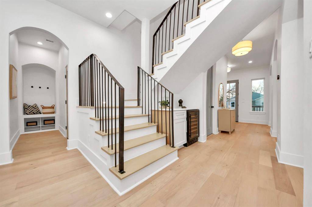 Ample archways lead into the mudroom, offering garage access and convenient hooks. The stunning staircase features thin metal rails, with illuminated lights highlighting each step as you ascend.