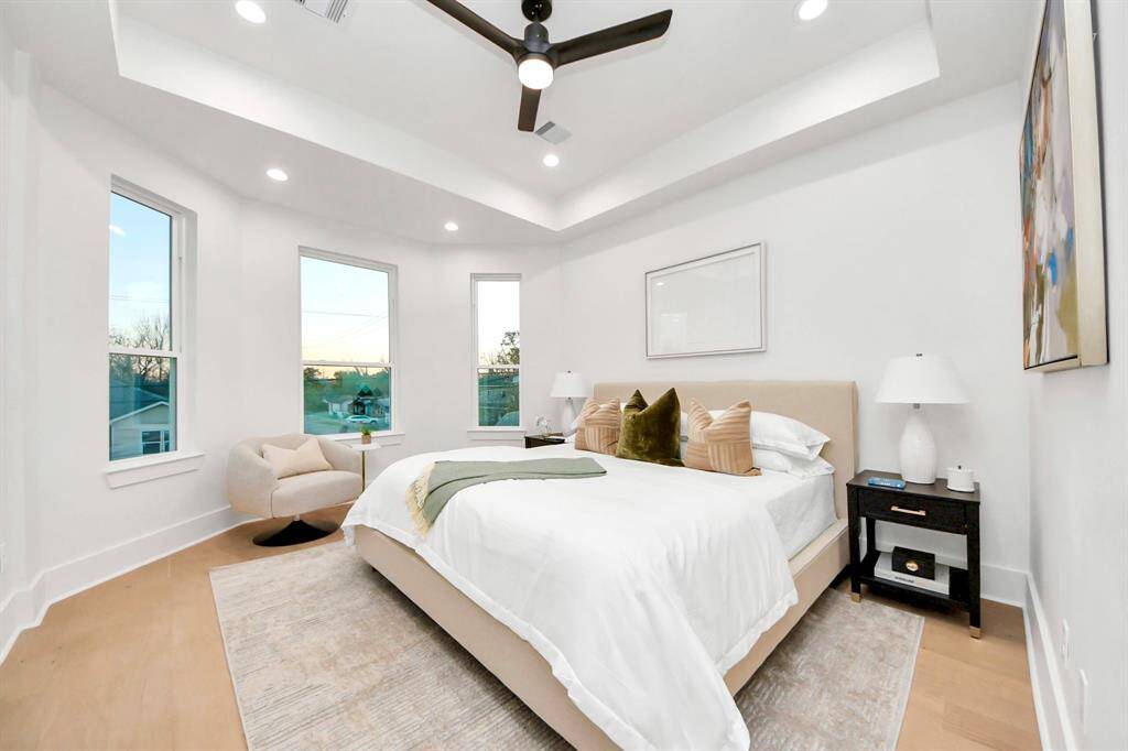 The primary suite awaits, with a recessed ceiling enhanced by ambient lighting. Three large windows flood the room with natural light, creating a bright and inviting space.