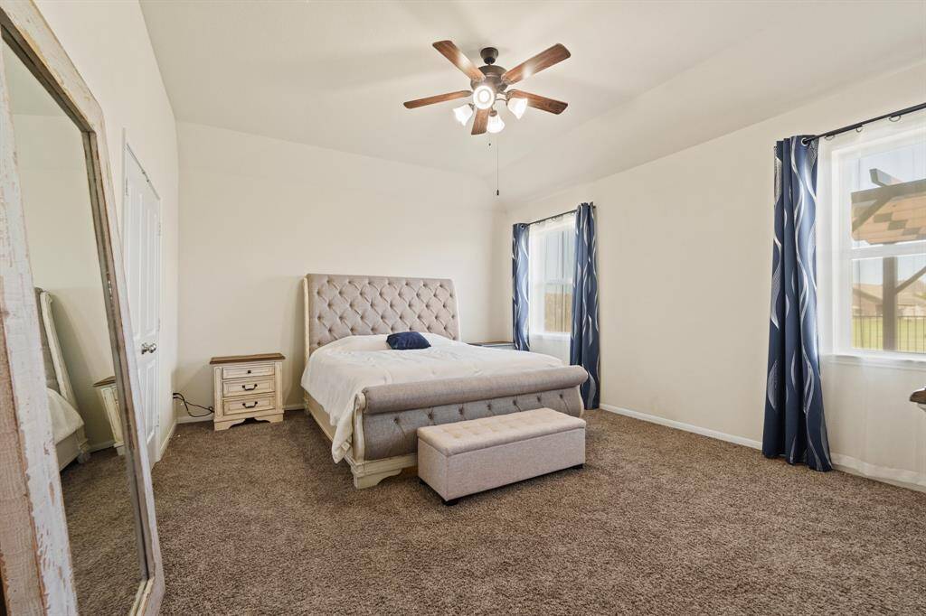 This spacious primary bedroom features large windows with stylish curtains, providing ample natural light. A ceiling fan adds comfort. Tons of space for your sanctuary!