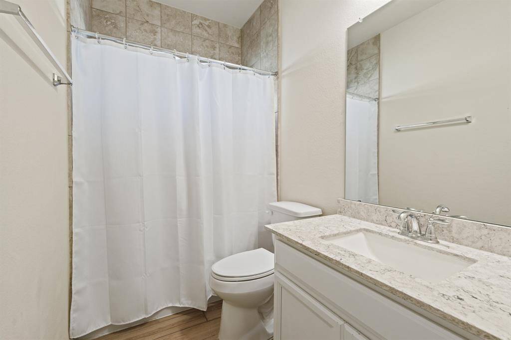This secondary bathroom features a clean, modern design with a granite countertop and a white vanity.