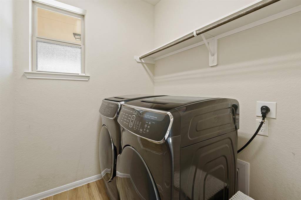 This photo features a compact laundry room with modern washer and dryer units. It has a small window for natural light and a shelf above for storage, offering efficient use of space.