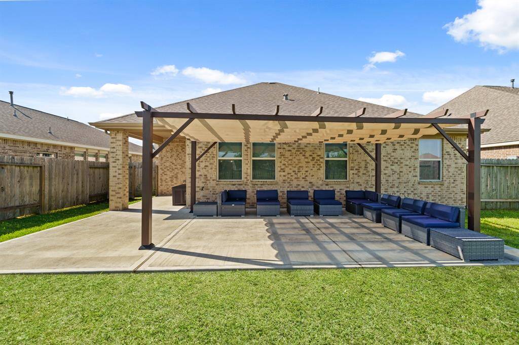 Spacious backyard with a large pergola over a concrete patio, featuring comfortable outdoor seating area. The well-maintained lawn and privacy fence provide a serene and inviting space for relaxation or entertaining.