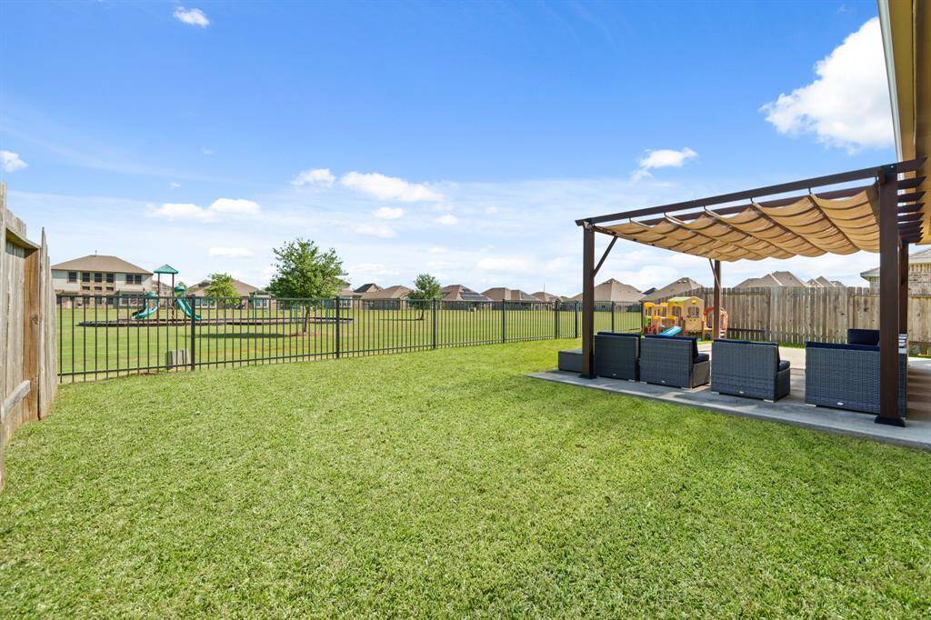 Spacious backyard with a well-maintained lawn, featuring a pergola with seating area for relaxation. The yard is fenced and adjacent to a playground, ideal for families.