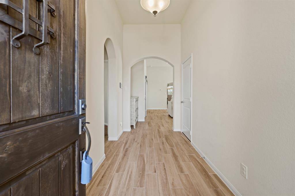 Welcome to a bright entryway featuring wood-look flooring and high ceilings. The hallway leads to an inviting living space, with arched doorways and a stylish light fixture enhancing its charm.