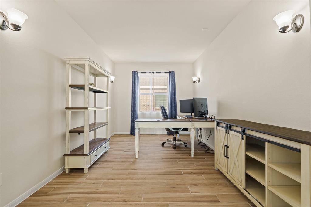This bright home office features wood-look flooring, and a large window with natural light.