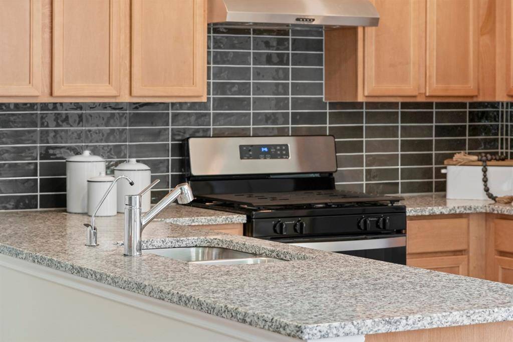 Featured here is the Whirlpool Black on Stainless Freestanding Gas Range with range hood, gorgeous granite counter in Luna Pearl, and coordinating backsplash.