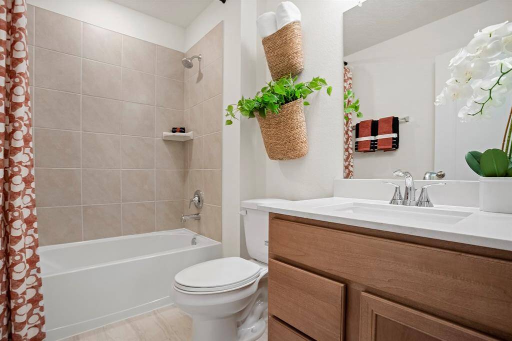 Secondary bath features porcelain tile flooring, bath/shower combo with tile surround, stained wood cabinets, light countertop, mirror, and chrome bathroom faucets!