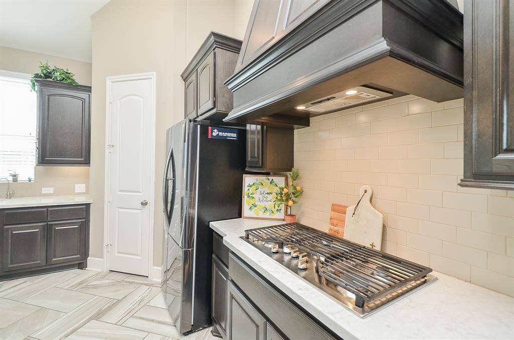 Simple light colored subway-style tile backsplash fills the space under the impressive, good looking exhaust. The nicely set-in cook top is also ready to go for Sunday brunch and/or fine dining in the evening.