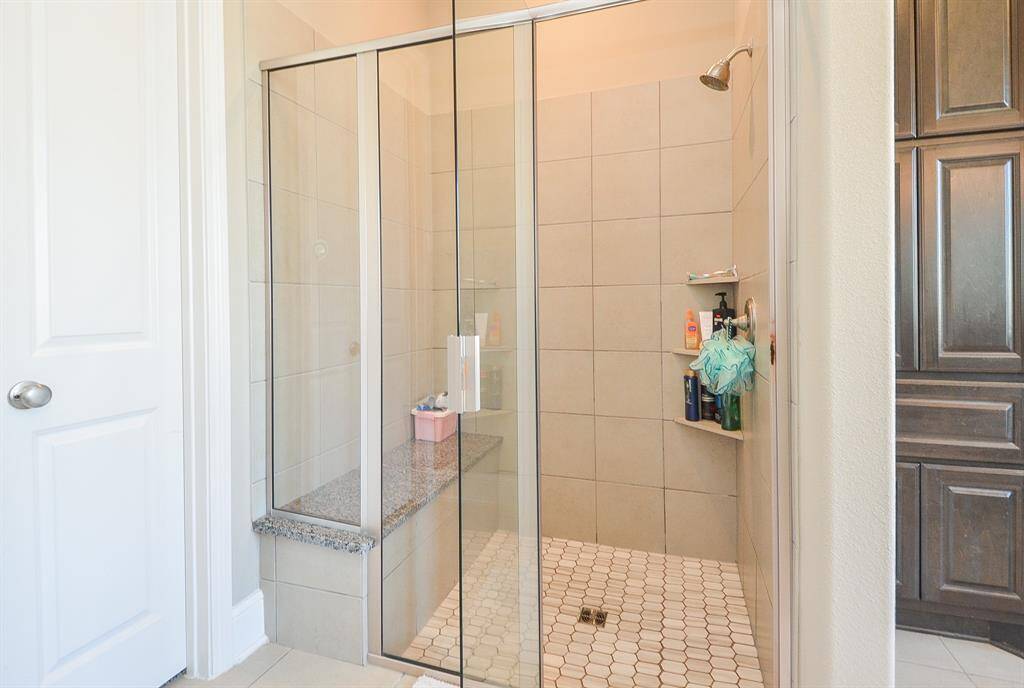 The ample walk-in, glass enclosed shower offers a welcomed bench and soothing tile surround.