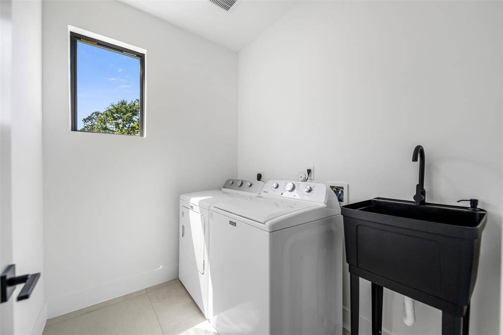 Bright laundry room with washer, dryer, and black utility sink.