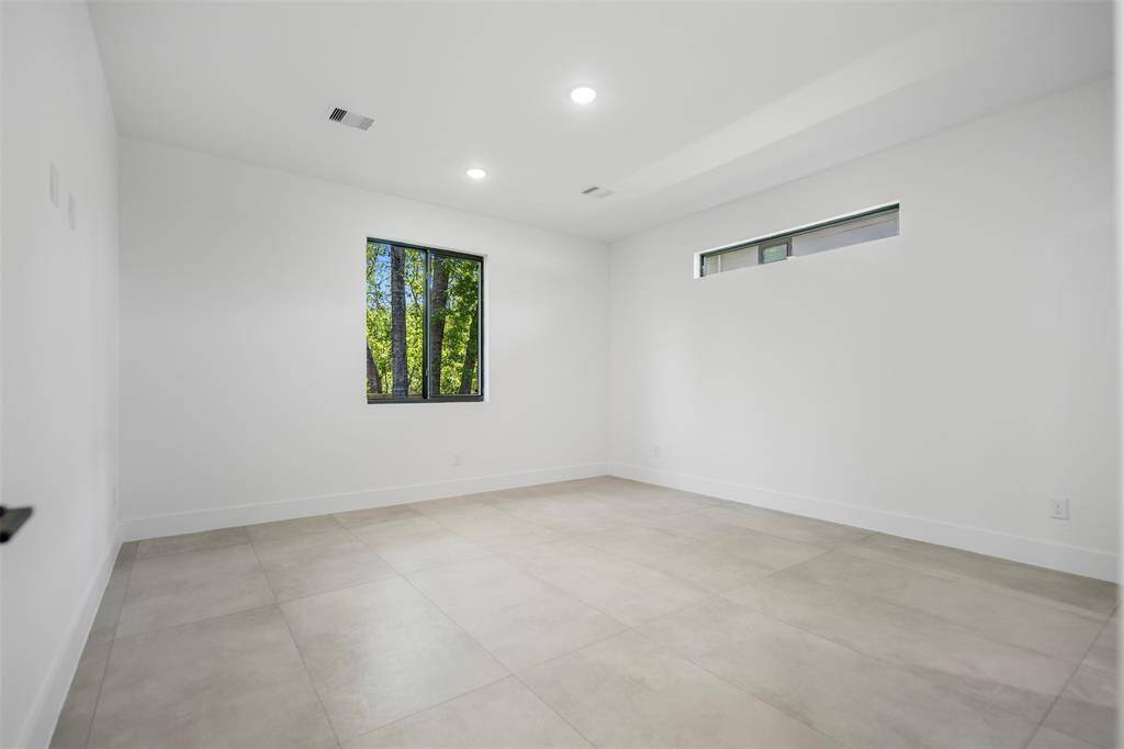 Unfurnished primary bedroom with large format tile flooring, clean white walls, and dual windows—including a horizontal clerestory—for a flood of natural light and modern character.