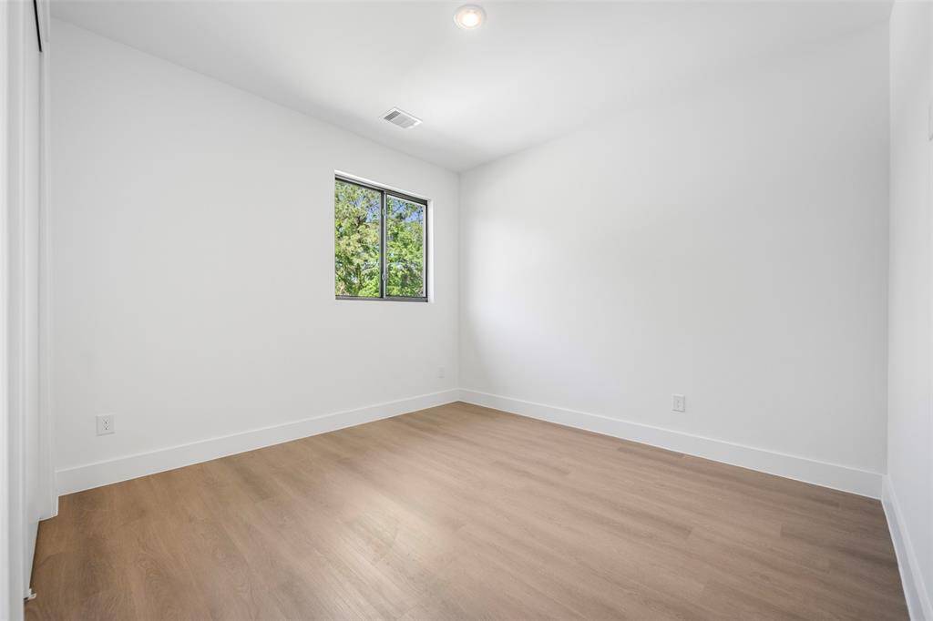 Spacious secondary bedroom with wide-plank wood-look flooring, a large window, and recessed lighting—perfect for a guest suite or family member.