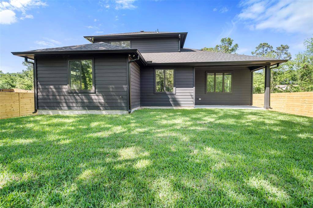 Rear elevation of the home showing the clean, modern exterior design with charcoal-toned siding, extended covered patio, and generous green space.