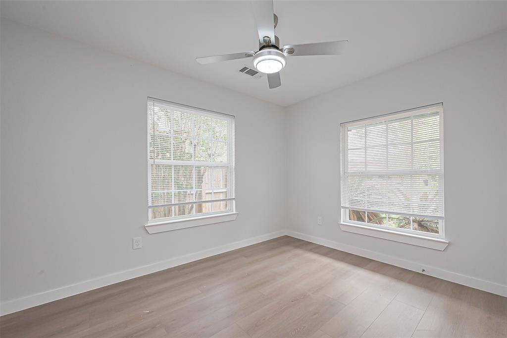 This bedroom feels airy and light, with oversized windows allowing daylight to flood the space, while the ceiling fan adds comfort on warmer days.