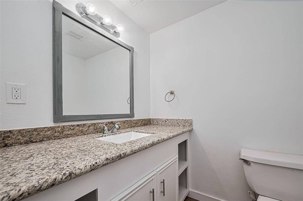 The half bathroom has a large vanity, featuring a wide mirror and ample under-cabinet storage, ideal for efficiency and style.
